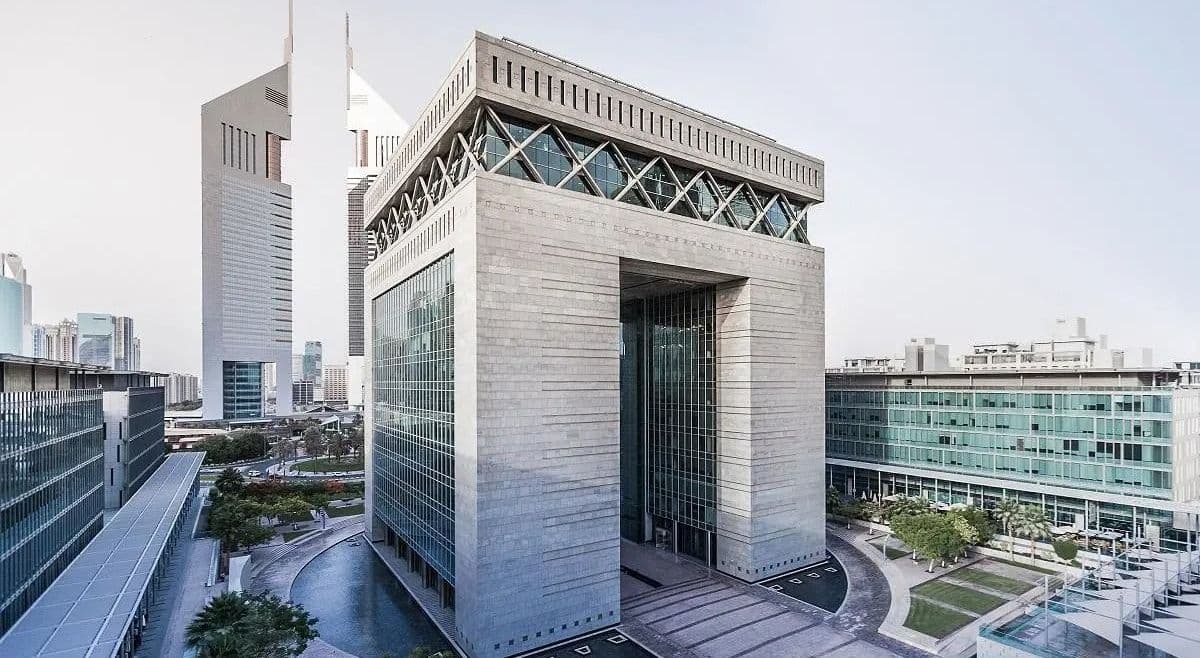 Modern stone-clad gateway-style office building at Dubai International Financial Centre, surrounded by glass-fronted offices, water features, and landscaped walkways on a clear day