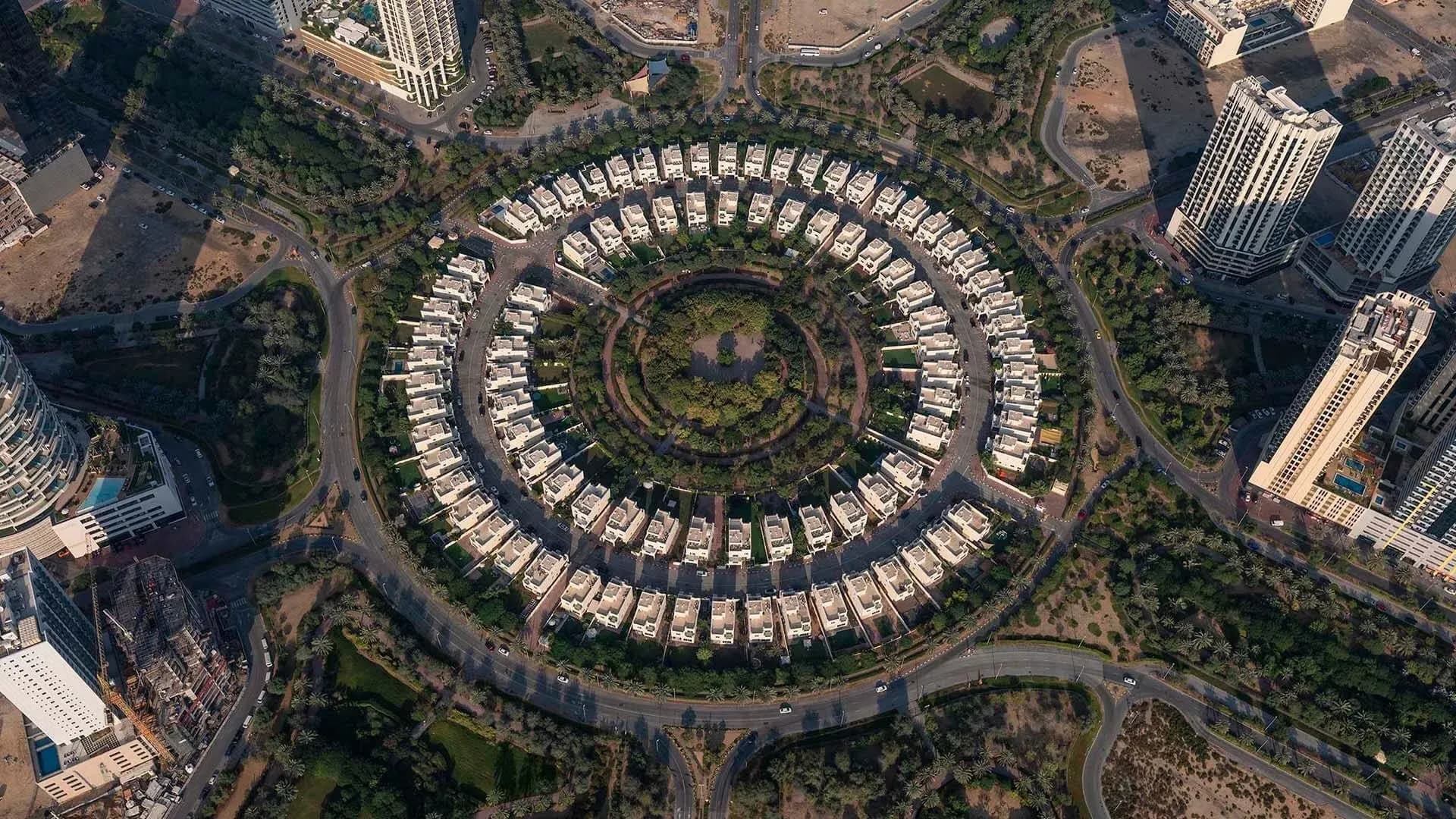 A direct top-down aerial view of JVC's circular layout, showing rows of villas around a central green park, surrounded by roads and high-rise buildings.