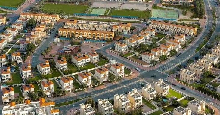 Aerial view of villas in Jumeirah Village Circle (JVC), Dubai surrounding a central landscaped park with nearby high-rise buildings.