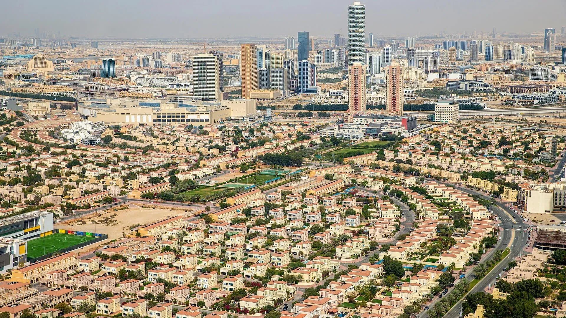 A panoramic aerial view of JVT’s expansive residential area, showcasing rows of uniform villas with terracotta roofs, surrounded by roads and high-rise buildings in the distance.