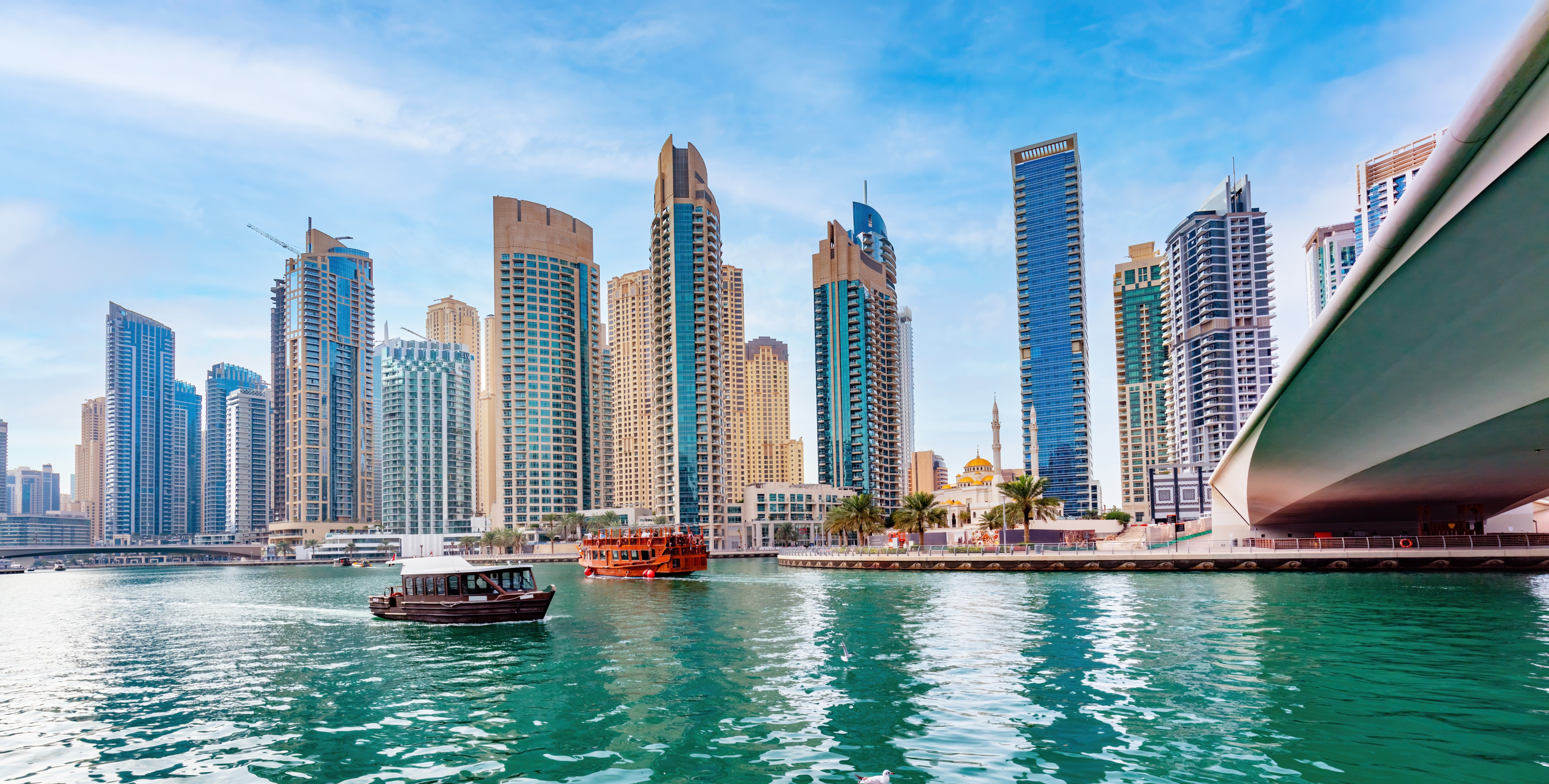 Dubai Marina waterfront with modern skyscrapers, a traditional wooden boat, and blue skies representing Dubai's growing real estate market