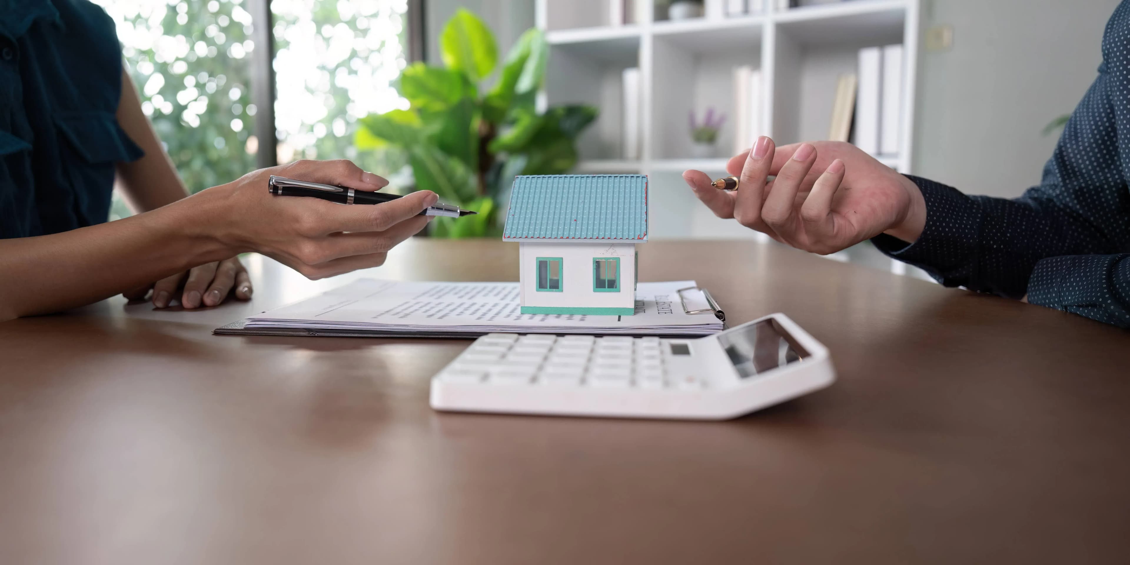 Two people reviewing a property contract with a model house and calculator before buying a tenanted property in Dubai