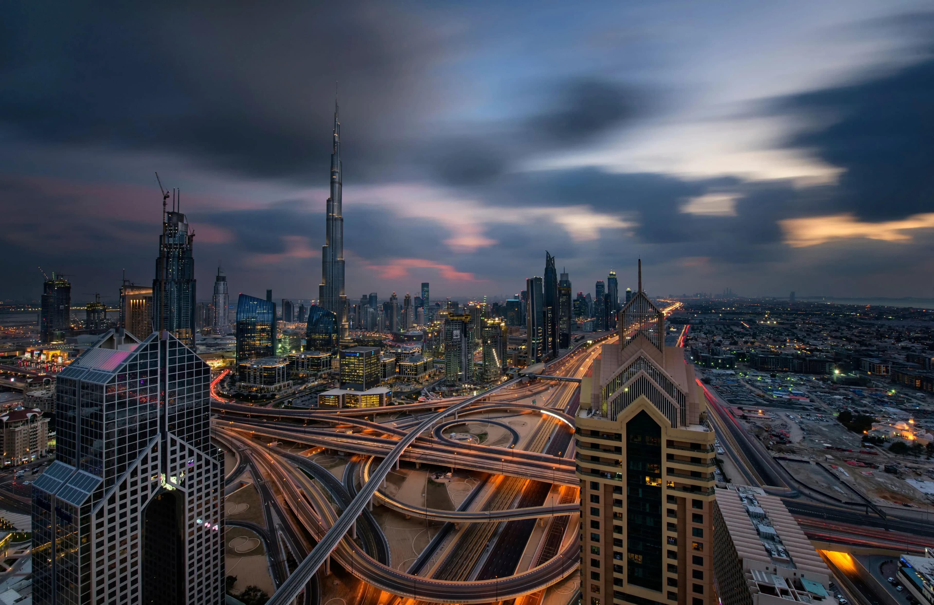An aerial shot of a city skyline during twilight, showcasing tall buildings and a network of roads with warm streetlights.