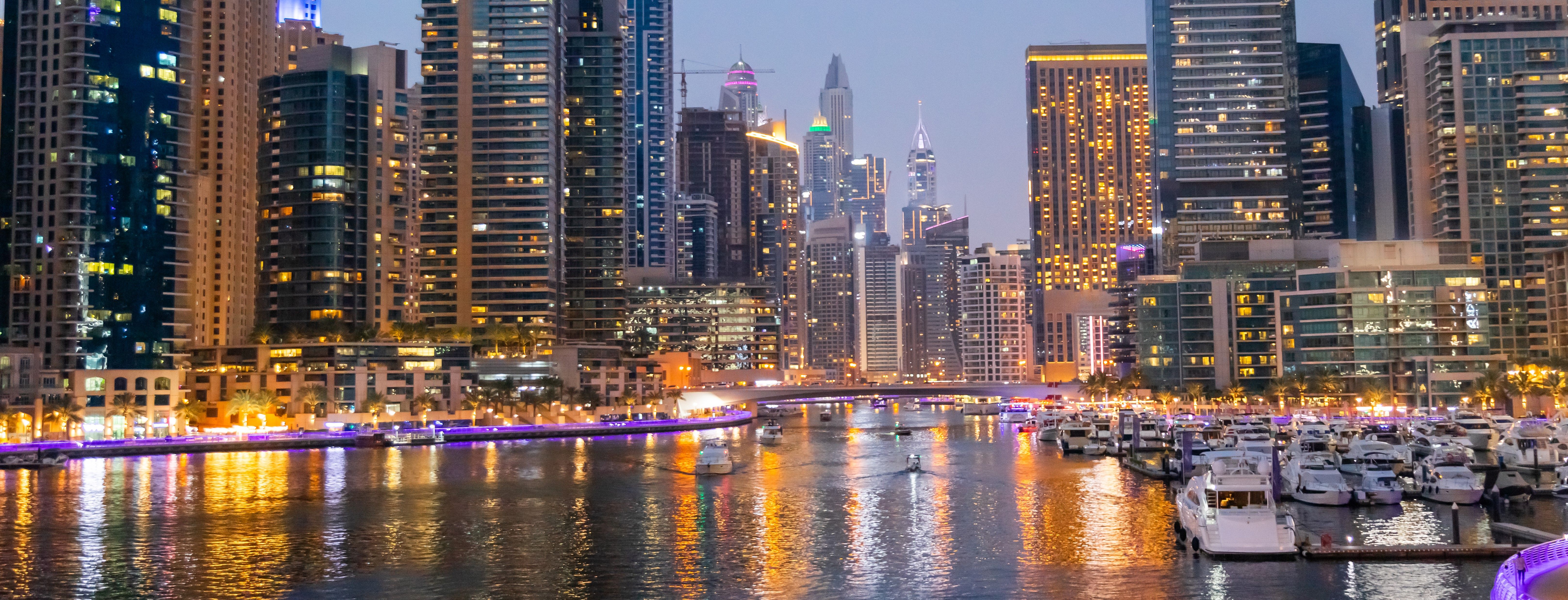 Stunning nighttime panoramic view of Dubai Marina with illuminated skyscrapers, luxury yachts, and vibrant waterfront reflections