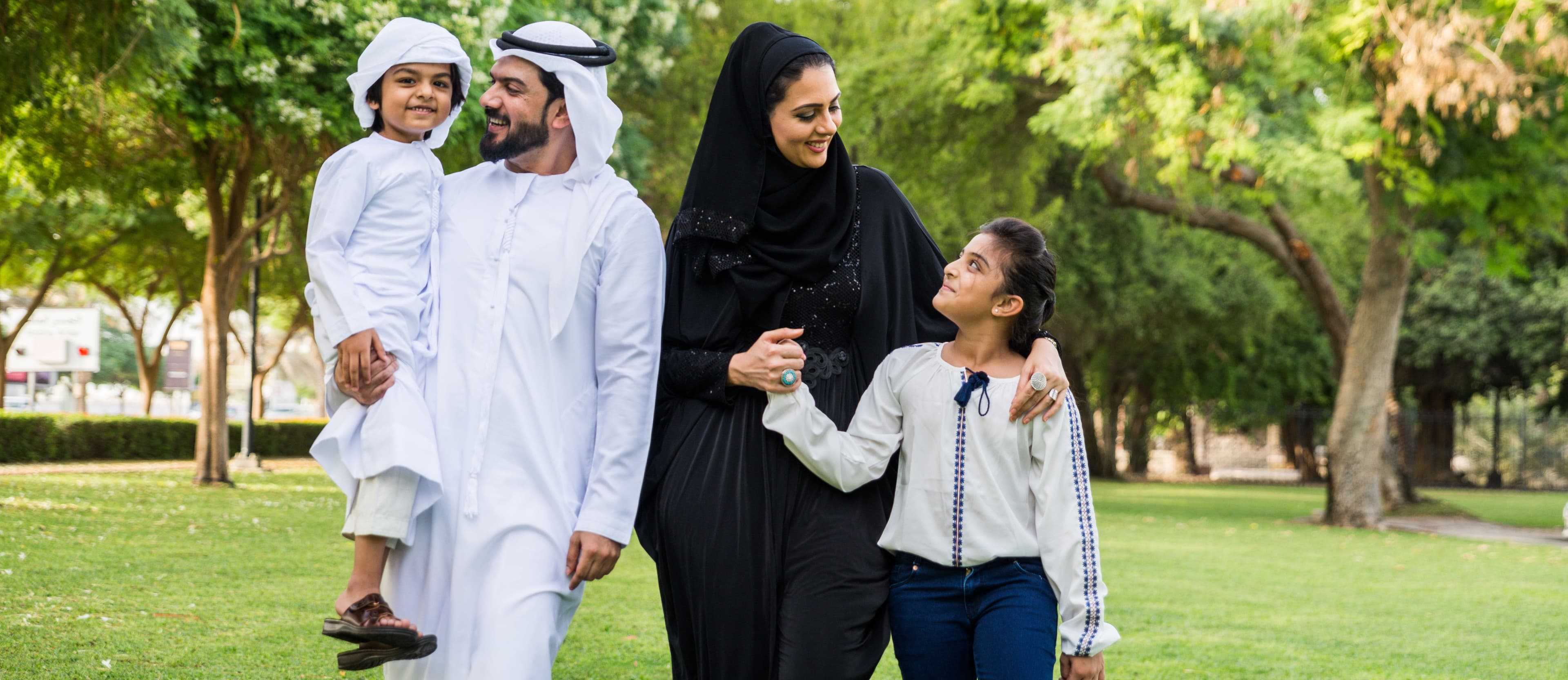Happy Emirati family walking together in a green park in Dubai.