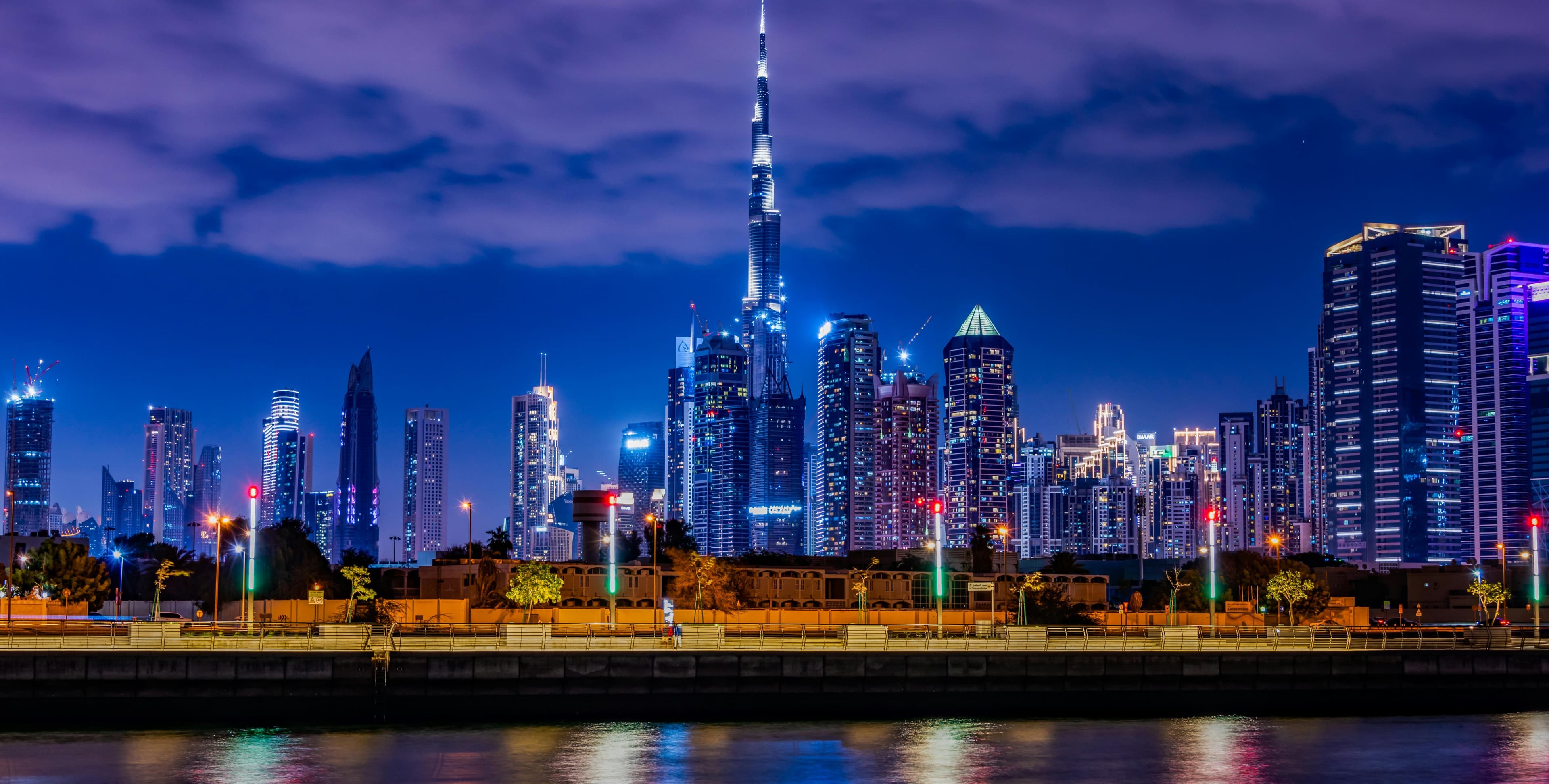 Night view of Dubai’s illuminated skyline with the Burj Khalifa and surrounding skyscrapers reflected in calm waterfront water.